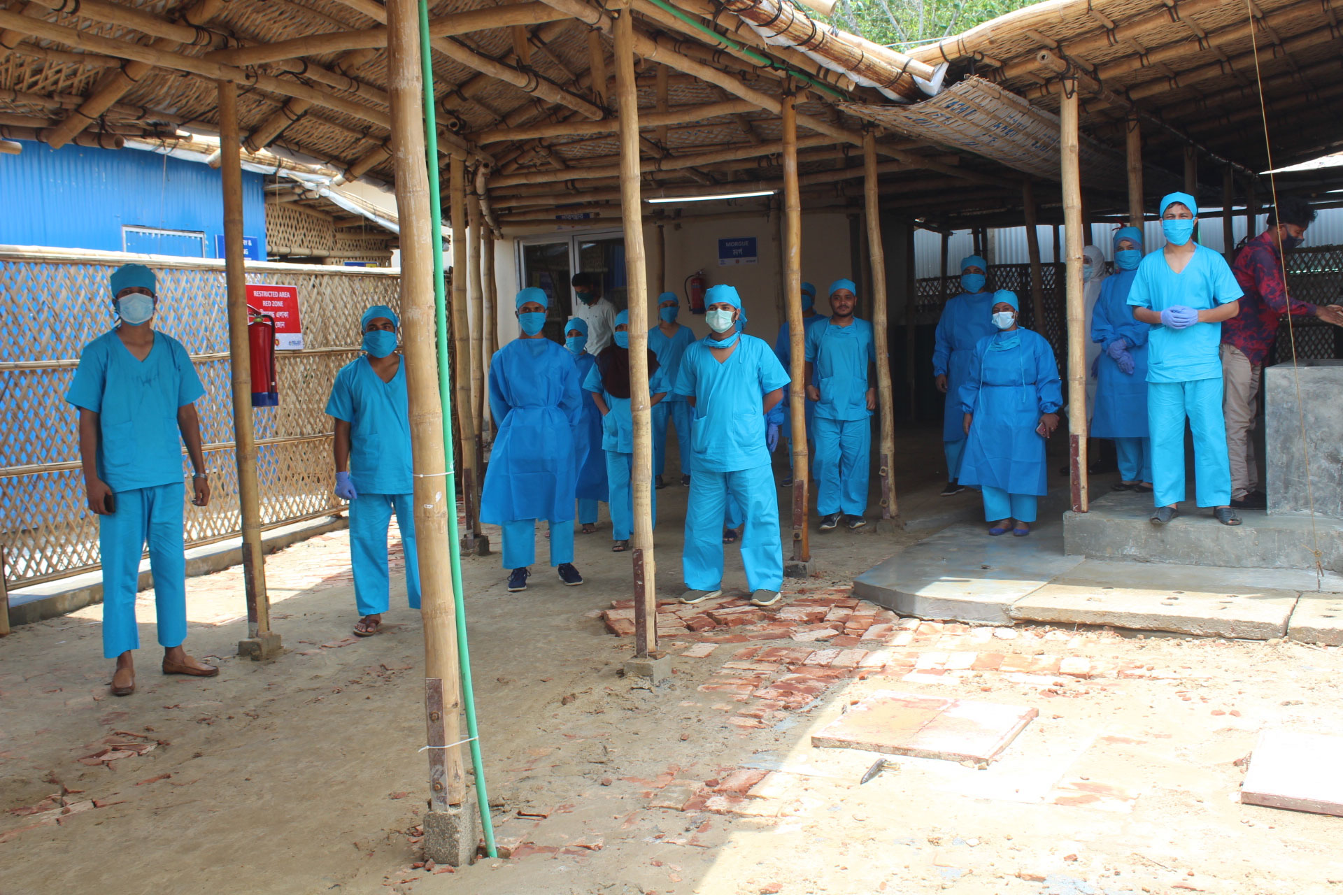 Medical personnel in blue scrubs and masks, standing outside a medical centre in the Cox's Bazar Settlement